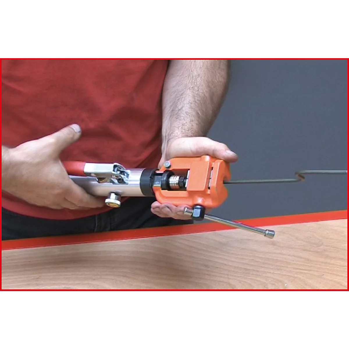 Person hält ein Crimpwerkzeug. Das orangefarbene Werkzeug ist auf einem Draht platziert, der durch das Werkzeug geführt wird.